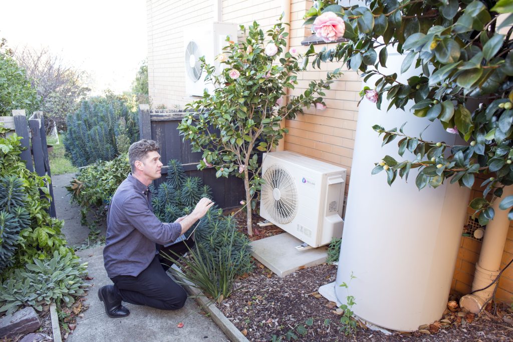 Cal, a qualified home energy assessor, assesses the energy efficiency of a heat pump hot water system during a home energy assessment.