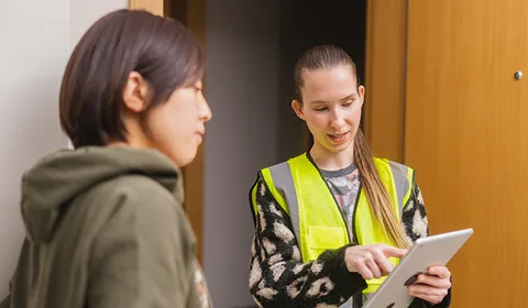 An accredited assessor at a resident's doorway, holding a tablet