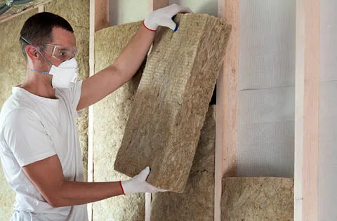 An installer fitting batt insulation between wall studs